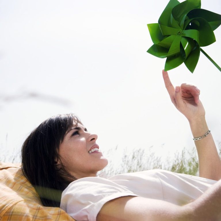 woman lying down on grass, smiling. Poking a green pin wheel